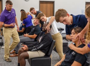 Instructor overseeing students palpating patients necks in technique classroom.